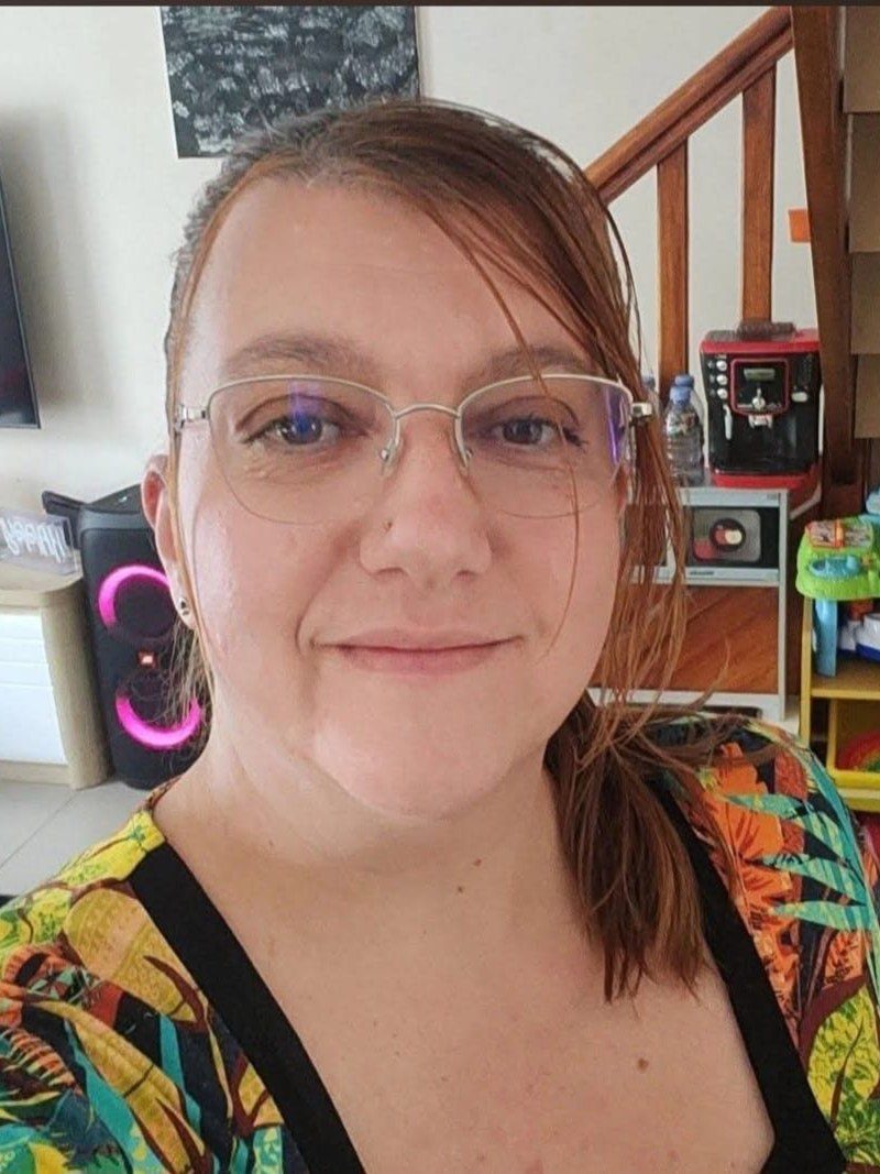 Aude, assistante maternelle agréée à Angerville, souriante dans sa pièce d'accueil, devant des étagères de jouets d'éveil colorés