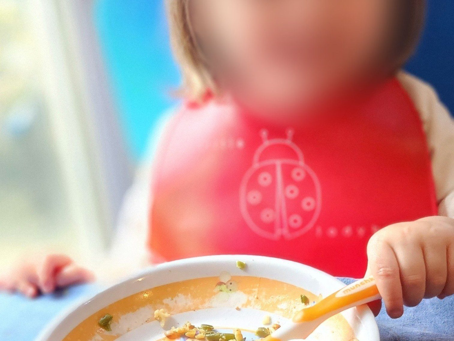 Une petite fille avec un bavoir mange seule à la cuillère des coquillettes aux haricots verts faites maison, chez l'assistante maternelle à Angerville